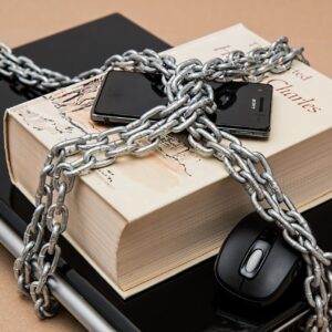 a laptop, a book, and a mobile phone wrapped in chains.