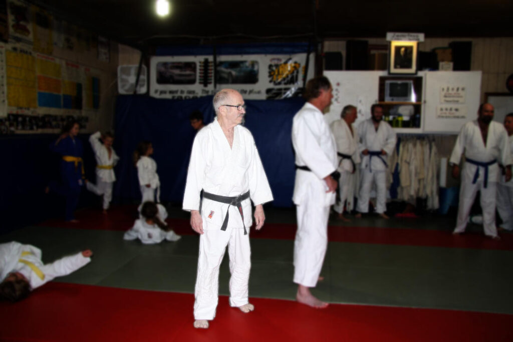 judo teacher standing in the middle of a dojo watching judoka practice breakfalls
