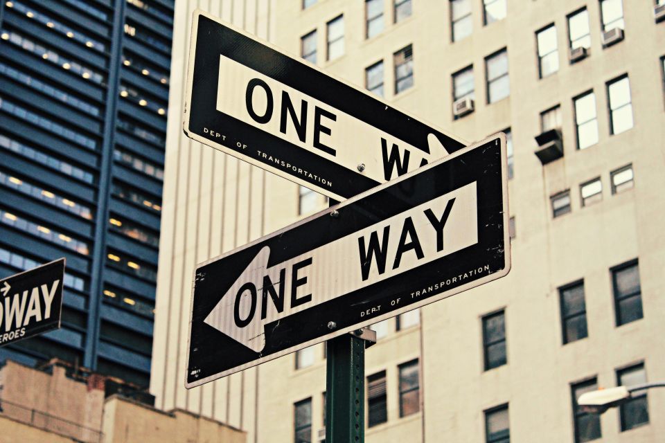 two one-way road signs pointing in different directions with buildings in the background.
